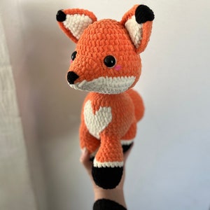May include: A crocheted orange fox plush toy with white accents and black eyes. The fox has a white heart on its chest.