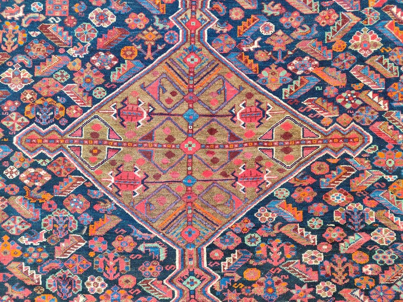 May include: A vintage rug with a geometric pattern in shades of blue, pink, red, and brown. The rug has a central diamond shape with intricate details and a border of smaller geometric shapes.