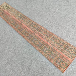 Pode incluir: Um tapete longo e estreito com um design persa tradicional. O tapete tem um fundo vermelho com padrões intrincados em verde e preto.