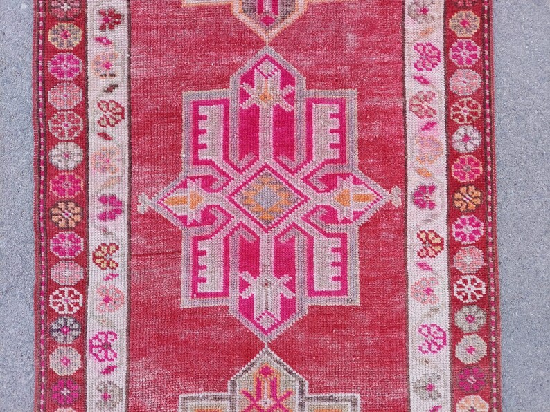 May include: A vintage Turkish runner rug with a pink and white geometric pattern. The rug has a faded, distressed look and features a central medallion design.