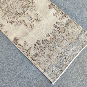 Puede incluir: Una alfombra de pasillo vintage con un patrón floral descolorido en tonos marrones, beige y grises. La alfombra tiene un borde deshilachado y un aspecto desgastado.