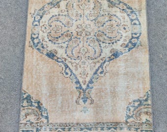 May include: A vintage rug with a faded beige background and a large blue and beige diamond pattern in the centre. The rug has a blue and beige border with a fringe.