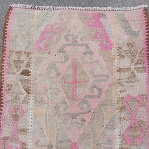 May include: A pink and brown patterned rug with a fringed edge. The rug has a geometric design with a central diamond shape.