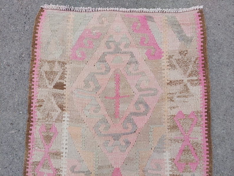 May include: A pink and brown patterned rug with a fringed edge. The rug has a geometric design with a central diamond shape.