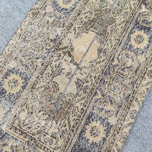Könnte beinhalten: Ein antiker Teppich mit einem abgenutzten, Vintage-Aussehen. Der Teppich hat ein zentrales Design in Beige und Braun, das von einem dunkelblauen Rand mit floralen und geometrischen Mustern umrahmt wird. Die Farben des Teppichs sind Beige, Braun und Blau.