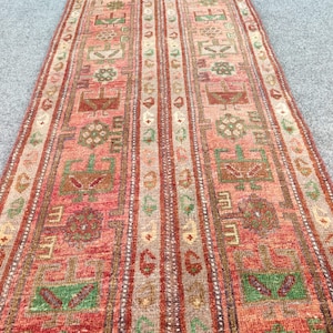 Pode incluir: Um tapete comprido e estreito com um design turco tradicional. O tapete é principalmente vermelho com detalhes verdes, castanhos e bege. O design apresenta padrões geométricos repetitivos e motivos florais.