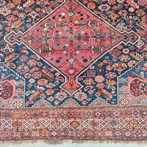 May include: A vintage Persian rug with a central diamond-shaped medallion in shades of pink, blue, and white. The rug has a dark blue background with intricate floral and geometric patterns.