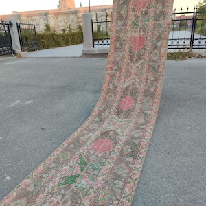 May include: A long, narrow rug with a pink and green floral pattern. The rug is laid out on a grey concrete surface.