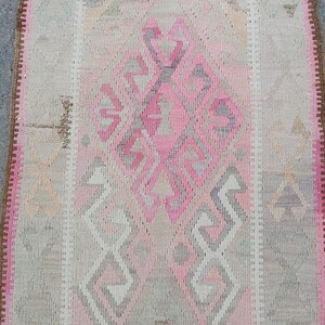 May include: A pink and gray patterned rug with a diamond-shaped design in the center. The rug has a fringe border.