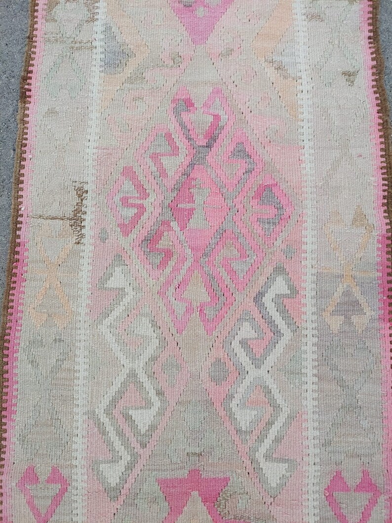 May include: A pink and gray patterned rug with a diamond-shaped design in the center. The rug has a fringe border.