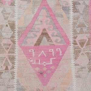 May include: A pink and brown patterned rug with a diamond-shaped design in the center. The rug has a fringe border and features a geometric pattern with Arabic script.