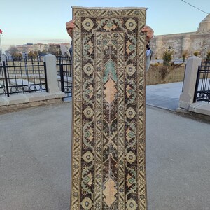 May include: A long, narrow rug with a traditional Turkish design. The rug has a dark brown background with intricate patterns in shades of beige, green, and blue.