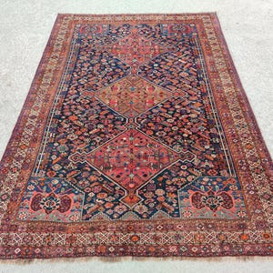 May include: A traditional Persian rug with a dark blue background and intricate floral patterns in shades of red, pink, and cream. The rug has a border with a geometric design.