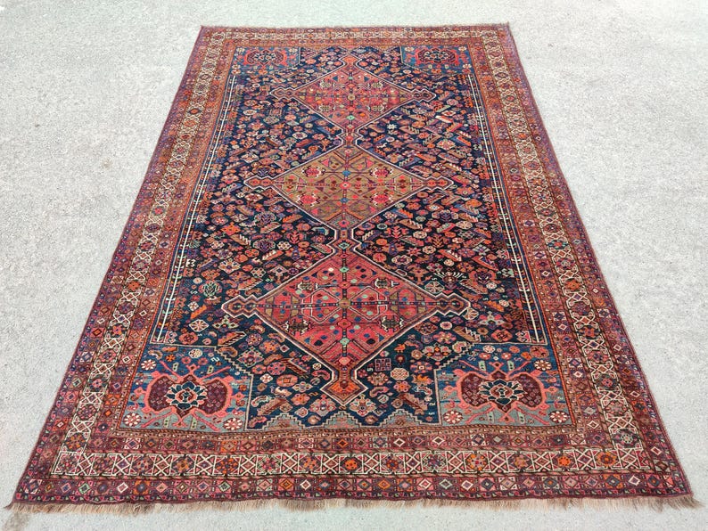 May include: A traditional Persian rug with a dark blue background and intricate floral patterns in shades of red, pink, and cream. The rug has a border with a geometric design.