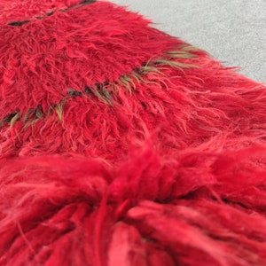 May include: A red and black shaggy rug with a long, fluffy pile. The rug has a striped pattern with black and brown stripes.