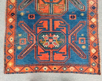 Op de afbeelding: Een traditioneel Turks tapijt met een blauwe achtergrond en ingewikkelde geometrische patronen in rood, oranje en geel. Het tapijt heeft een rand met een herhalend ruitpatroon.
