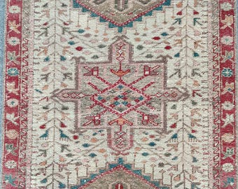 May include: A vintage rug with a cream background and a central medallion in shades of red, blue, and green. The rug has a border with a repeating pattern of red, white, and blue.