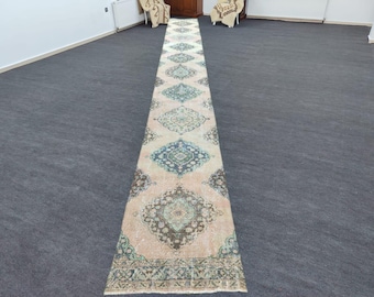 May include: A long, rectangular rug with a cream background and intricate floral patterns in shades of blue, green, and brown. The rug has a fringed edge and is laid out on a grey carpet.