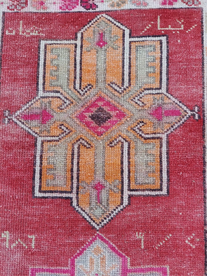 May include: A vintage Turkish rug with a red background and a central design featuring a cross with intricate details in shades of orange, green, and black.