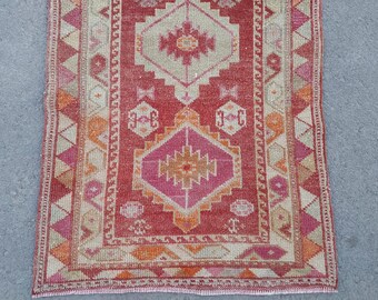 Puede incluir: Una alfombra turca vintage con fondo rojo y intrincados patrones geométricos en tonos rosa, naranja y beige. La alfombra tiene un borde con flecos.