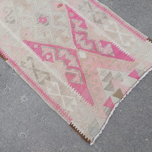 May include: A pink and beige patterned runner rug with fringe on the edges. The rug has a geometric design with a diamond pattern.