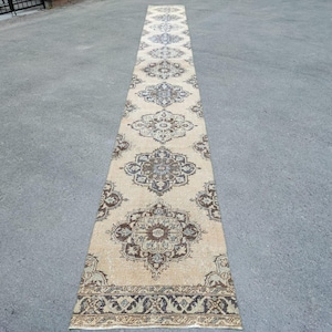 May include: A long, cream-coloured rug with a traditional floral pattern in shades of brown and beige. The rug has a fringed edge and is perfect for adding a touch of elegance to any room.