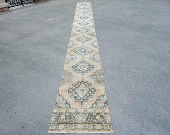 May include: A long, beige runner rug with a traditional, intricate pattern in shades of blue, green, and brown. The rug has a faded, vintage look and is perfect for adding a touch of elegance to any room.