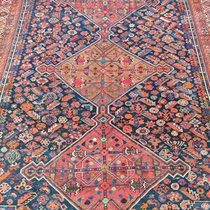 May include: A vintage Persian rug with a deep blue background and intricate geometric patterns in shades of pink, red, and beige. The rug features a central medallion and repeating motifs throughout.