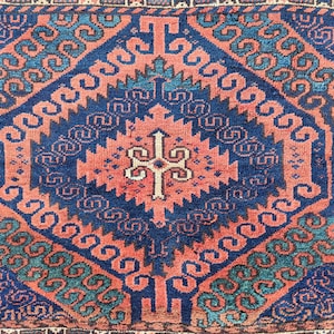 May include: A traditional rug with a blue and red geometric pattern. The rug has a central design with a cross shape and is surrounded by repeating patterns of swirls and lines.