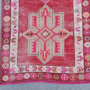 May include: A vintage Turkish rug with a pink and white geometric pattern. The rug has a pink fringe and a faded red background.