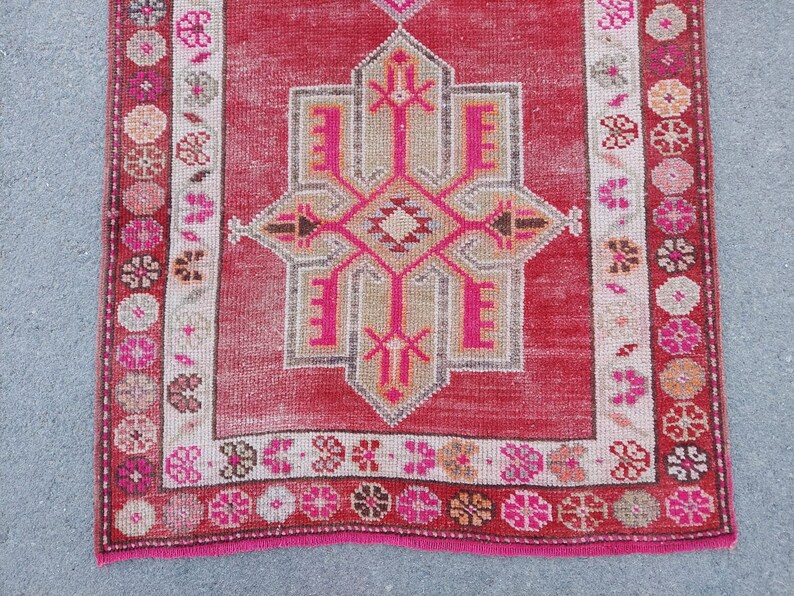May include: A vintage Turkish rug with a pink and white geometric pattern. The rug has a pink fringe and a faded red background.