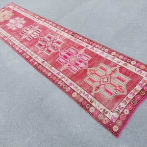 May include: A long, narrow red runner rug with a white border and intricate pink and beige geometric patterns.