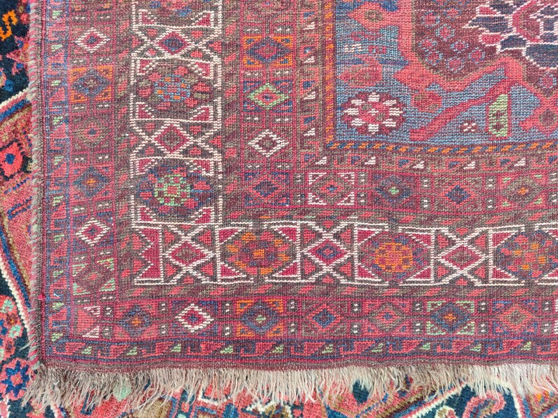 May include: Close-up of a red, blue, and white patterned rug with a fringe border. The rug has a geometric design with intricate details.