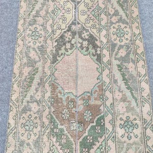 Peut inclure: Tapis rectangulaire vintage à l'aspect vieilli. Le motif central est composé de marron, rose et vert, encadré de bordures à motifs floraux et géométriques. La palette de couleurs est discrète, avec des tons terreux. Le tapis semble être noué à la main.