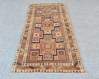 May include: A rectangular area rug featuring a central geometric medallion design in shades of dusty rose, navy blue, and tan. The rug is decorated with repeating square and diamond motifs throughout the field, framed by a wide, intricate border.