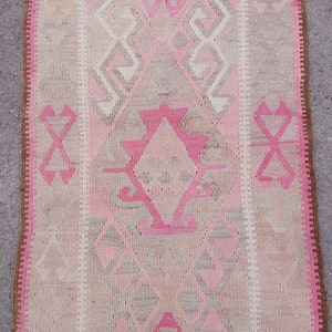 May include: A pink and beige patterned rug with a fringe border. The rug has a traditional design with geometric shapes and a central diamond.