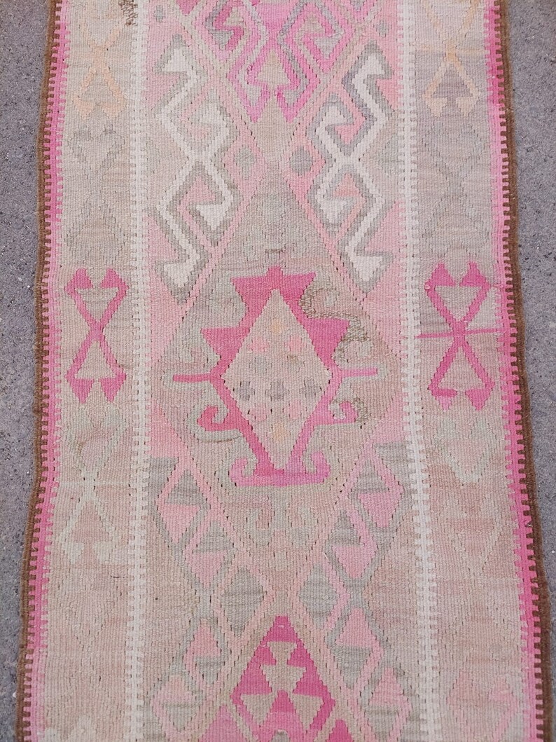 May include: A pink and beige patterned rug with a fringe border. The rug has a traditional design with geometric shapes and a central diamond.