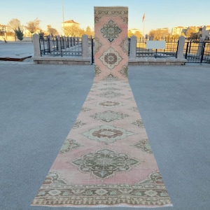 May include: A long, pink and green patterned rug with intricate designs. The rug is laid out on a grey concrete surface.