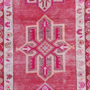 May include: A vintage pink and white runner rug with a geometric pattern. The rug has a faded look and is made of wool.