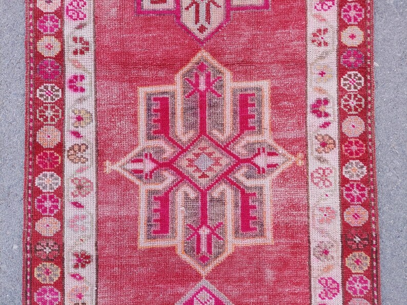 May include: A vintage pink and white runner rug with a geometric pattern. The rug has a faded look and is made of wool.