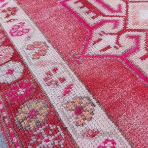May include: Close-up of a pink and white patterned rug with a geometric design. The rug has a fringed border and is made of woven fibres.