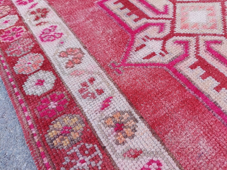 May include: Close-up of a pink and white patterned rug with a geometric design. The rug has a fringed border and is made of woven fibres.
