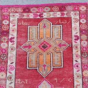May include: A vintage Turkish rug with a red background and a central medallion in shades of orange, pink, and brown. The rug has a floral border in shades of pink, white, and brown.