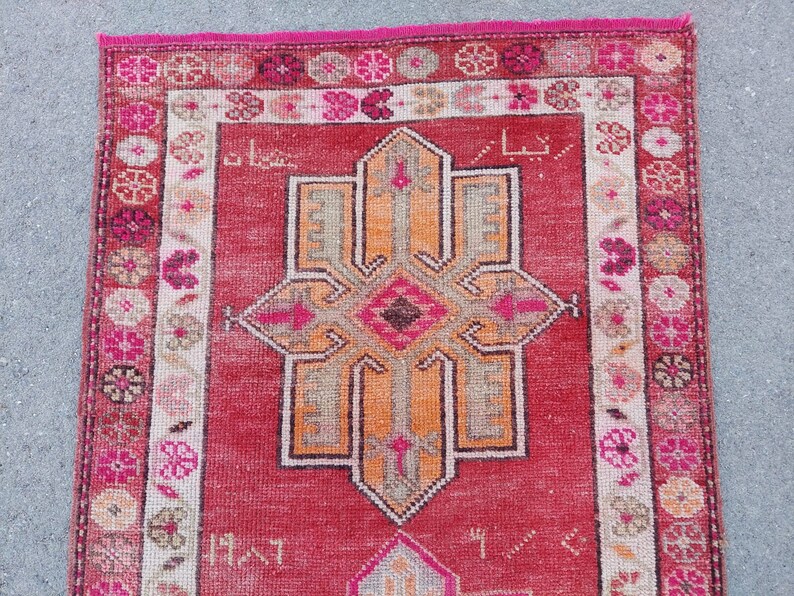 May include: A vintage Turkish rug with a red background and a central medallion in shades of orange, pink, and brown. The rug has a floral border in shades of pink, white, and brown.