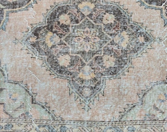 May include: A vintage rug with a faded pink background and a dark brown and blue geometric pattern. The rug has a distressed look and a worn border.
