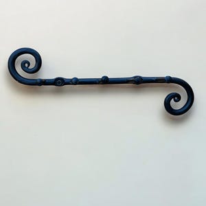Könnte beinhalten: Schwarzer Wand-Kleiderbügel aus Metall mit zwei dekorativen Enden in Form von Spiralen.