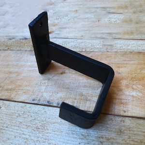 May include: Black metal wall mount hook with a square shape. The hook is designed to hold items like towels or coats.