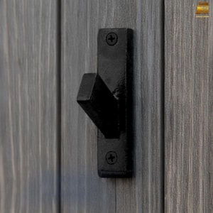 May include: Black metal hook with a square base and a single hook extending out. The hook is mounted on a wooden surface.