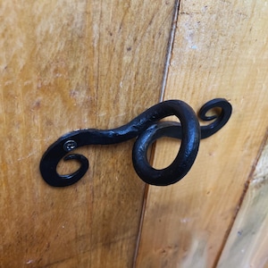 Puede incluir: Pomo de puerta de metal negro con un diseño decorativo de espiral. El pomo está fijado a una puerta de madera.