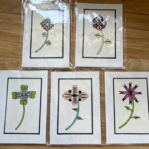 May include: Five cards with black borders, each featuring a different colorful flower design. The flowers are stylized and geometric, with intricate patterns and details. The cards are blank inside, perfect for writing messages or notes.